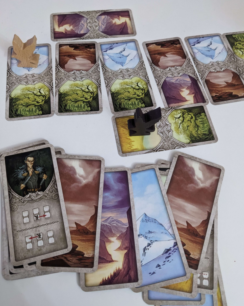 A photo of card gameplay from the card game Odin's Ravens. A set of cards are lined up with crow player pieces placed ontop along with a discard deck that is splayed to show off the last moves that won the game.